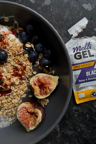 Bowl of granola with fruits and a Melli Gel energy bar on a dark surface